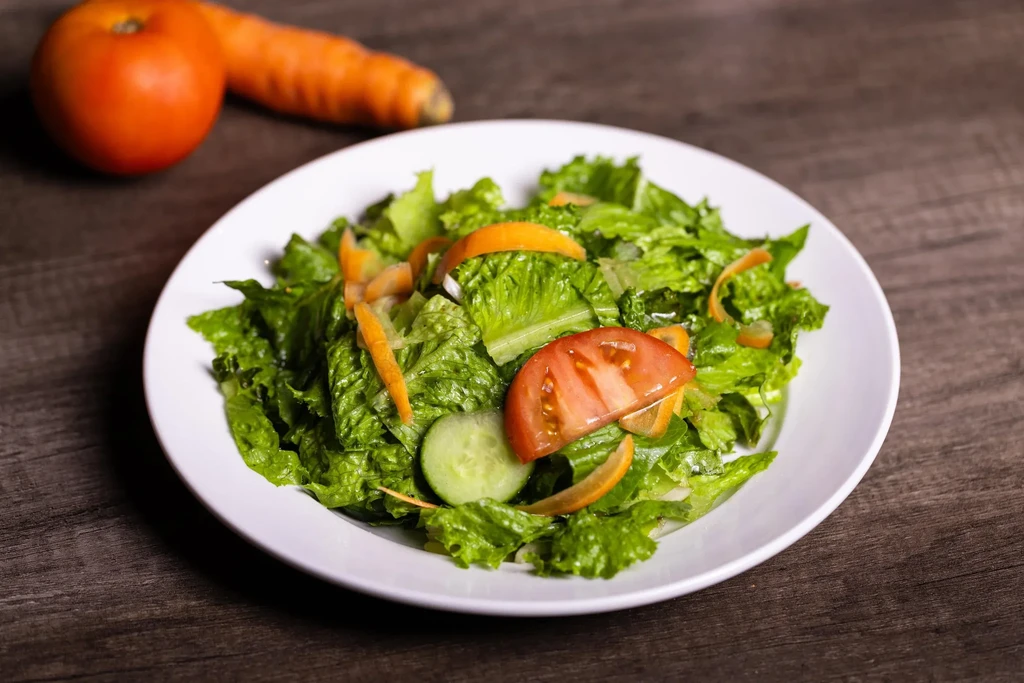 Fresh green salad with lettuce, tomato, cucumber, carrots on wood.