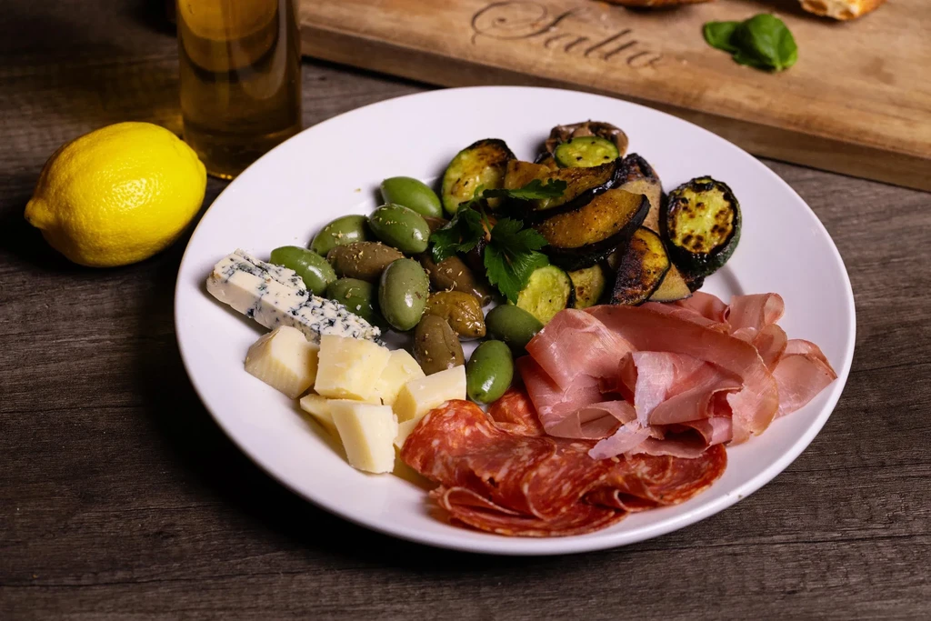 Charcuterie plate with meats, cheeses, olives, grilled vegetables, lemon, beer.
