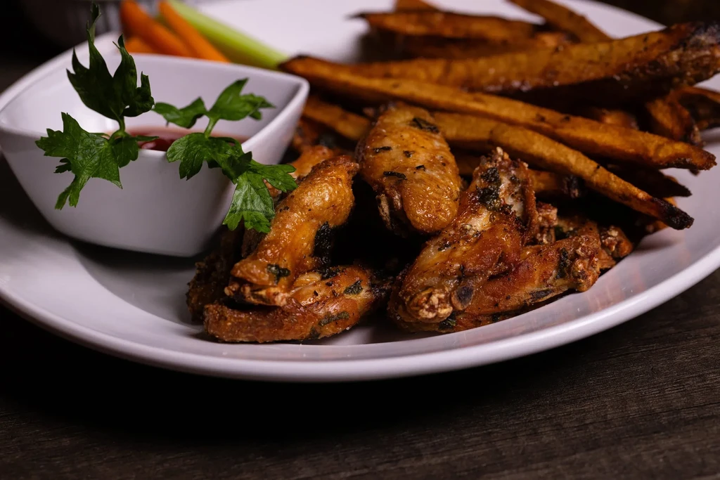 Crispy chicken wings, dark fries, red sauce, and fresh parsley.