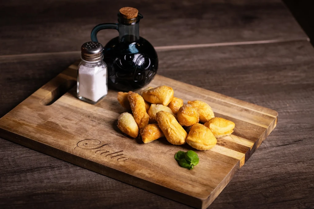 Golden-brown dough pieces, salt shaker, oil bottle, basil on wooden board.