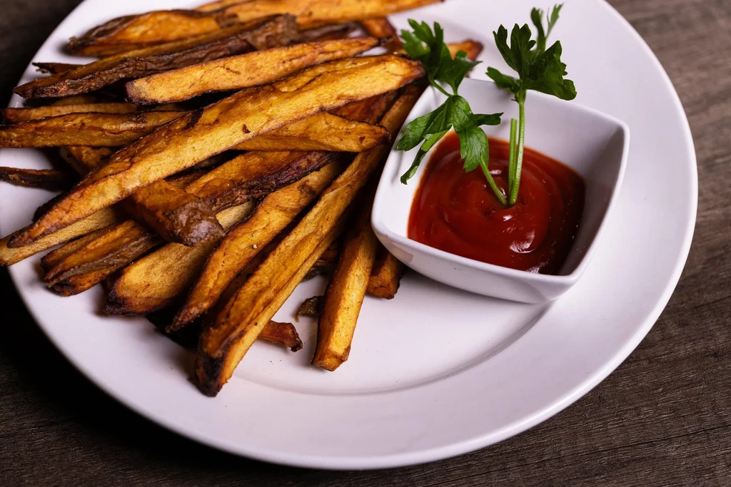 Rustic french fries with ketchup and parsley on a white plate.
