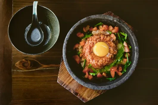 Korean bibimbap with raw egg yolk in a dark stone bowl on wood.