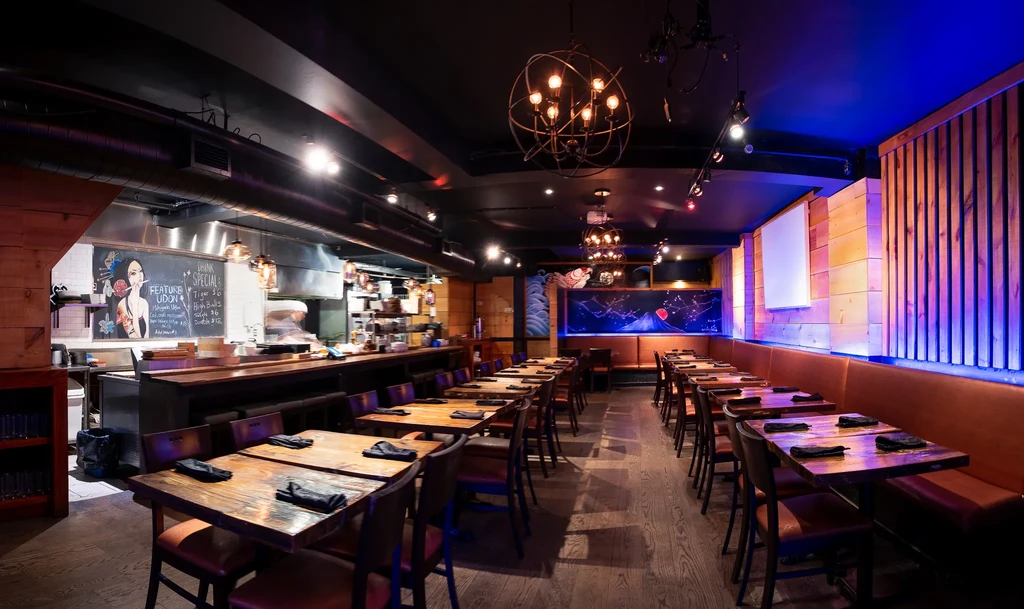 Modern, empty restaurant interior with open kitchen, udon chalkboard, and mural.