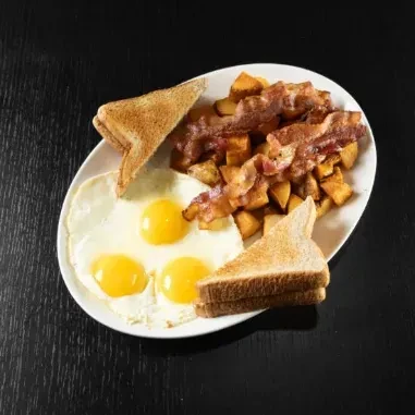 Plate of sunny-side-up eggs, crispy bacon, home fries, and toast.