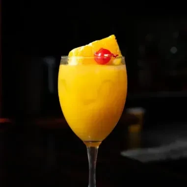 Stemmed glass with yellow-orange blended drink, orange wedge, and cherry.