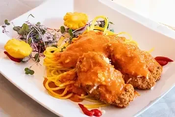 Breaded cutlets, spaghetti, creamy orange sauce, and colorful garnishes.