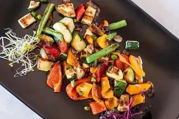 Colorful grilled vegetables and halloumi cheese on a dark plate.