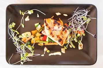 Overhead view of char-marked grilled protein, diced vegetables, microgreens.
