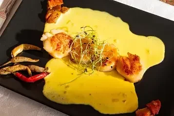 Seared scallops with yellow sauce, microgreens, chili peppers, and seafood.