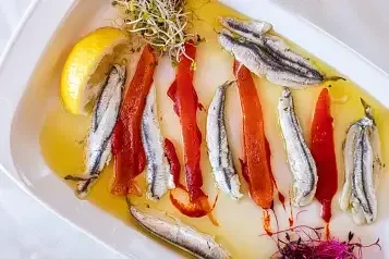 Close-up of fish fillets, red peppers, lemon, sprouts in olive oil.