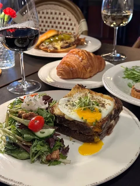 Overhead view of a Croque Madame with runny egg, side salad, and wine.