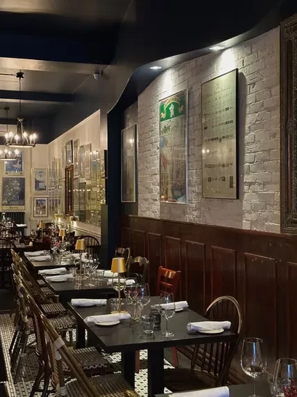 Elegant, narrow restaurant with brick walls, art, set tables, and patterned floor.