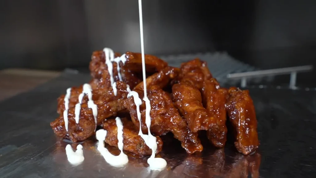 Glazed chicken wings drizzled with white sauce on a metallic tray.