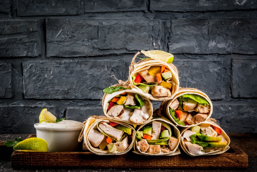 Stacked open chicken and vegetable wraps, tied with twine, with dipping sauce.