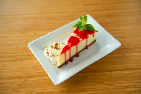 Cheesecake slice topped with berry sauce, mint, and whipped cream.