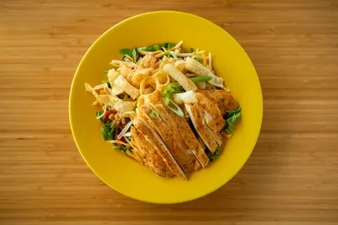 Top-down view of colorful grilled chicken salad on a yellow plate.