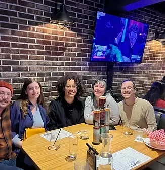 Five smiling people at a table with drinks in a dimly lit bar.