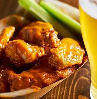 Buffalo wings in paper boat, with celery sticks and beer.