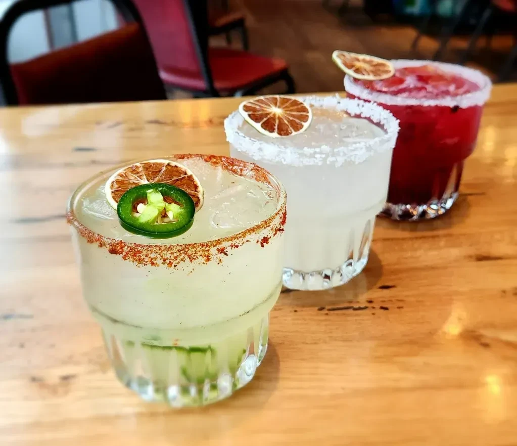 Three colorful cocktails with garnishes on a wooden table.