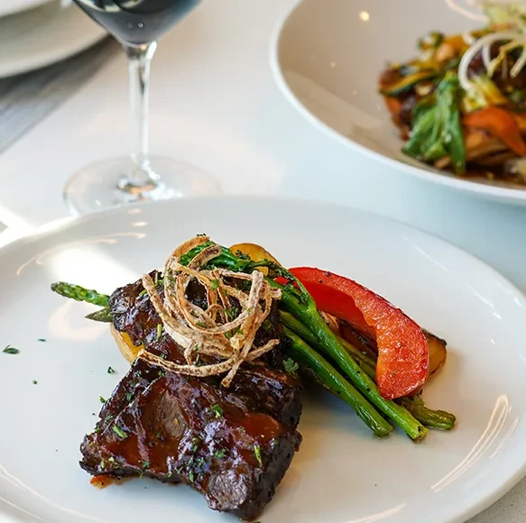 Braised meat, asparagus, potato wedges, and crispy fried onions on a plate.