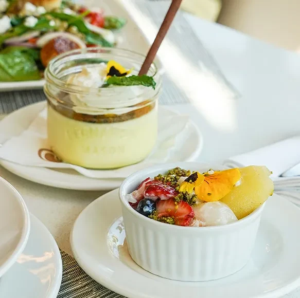 Colorful fruit salad and layered parfait with spoon on table.