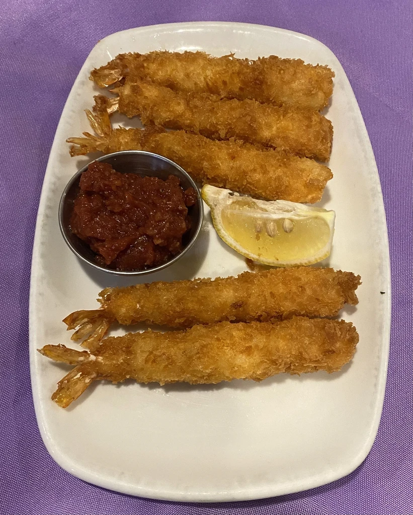 Six golden breaded shrimp, dipping sauce, and lemon on purple.