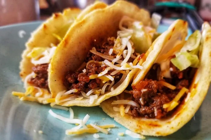 Three soft tacos with seasoned meat, two cheeses, and lettuce.