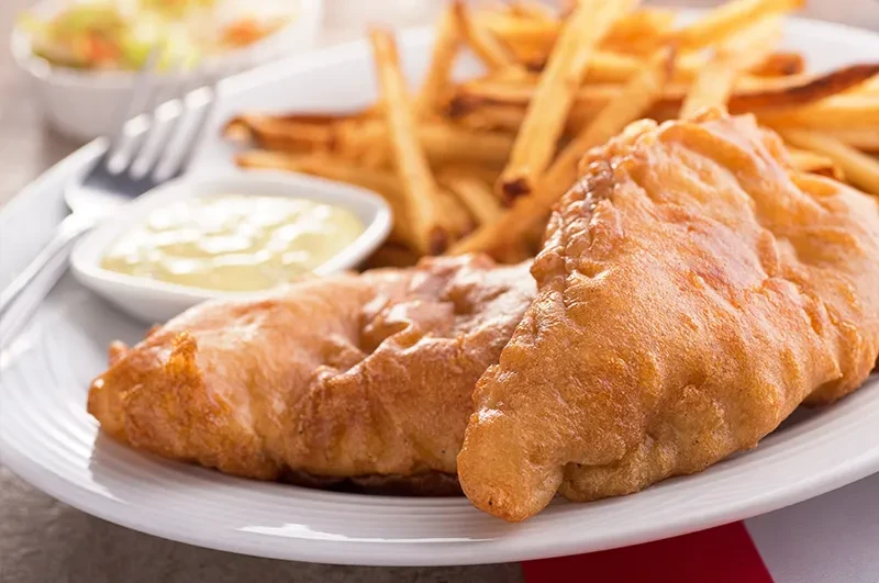 Close-up of golden-brown fish and chips with tartar sauce and a fork.