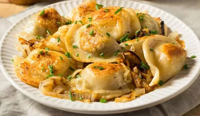 Pan-fried dumplings with chives and caramelized onions on a white plate.