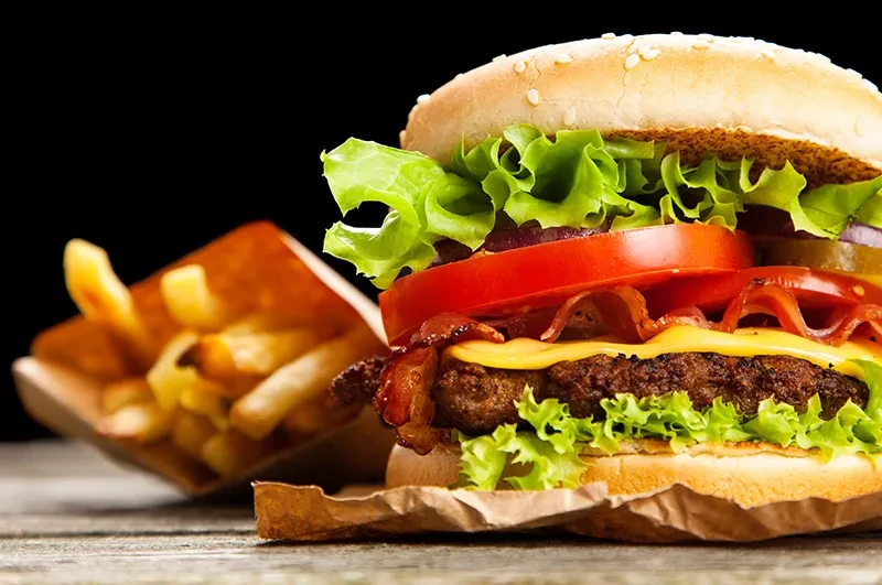 Close-up of a stacked burger with bacon, cheese, and fries.