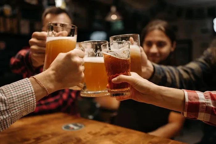 Diverse hands clink four glasses of beer and one dark drink.