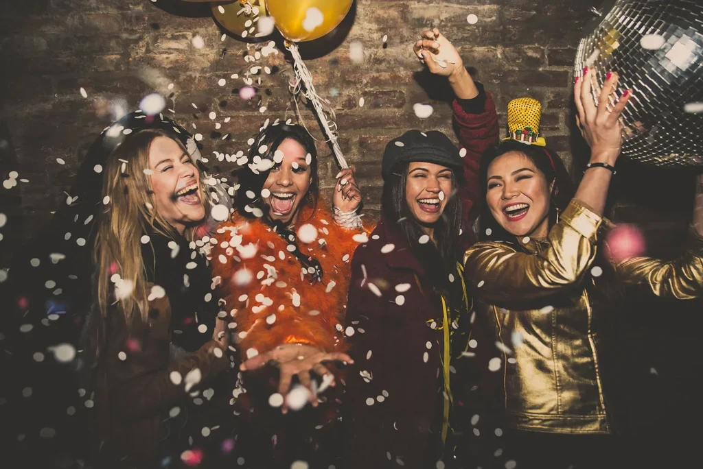 Four young women laughing amidst confetti, one holding a disco ball.