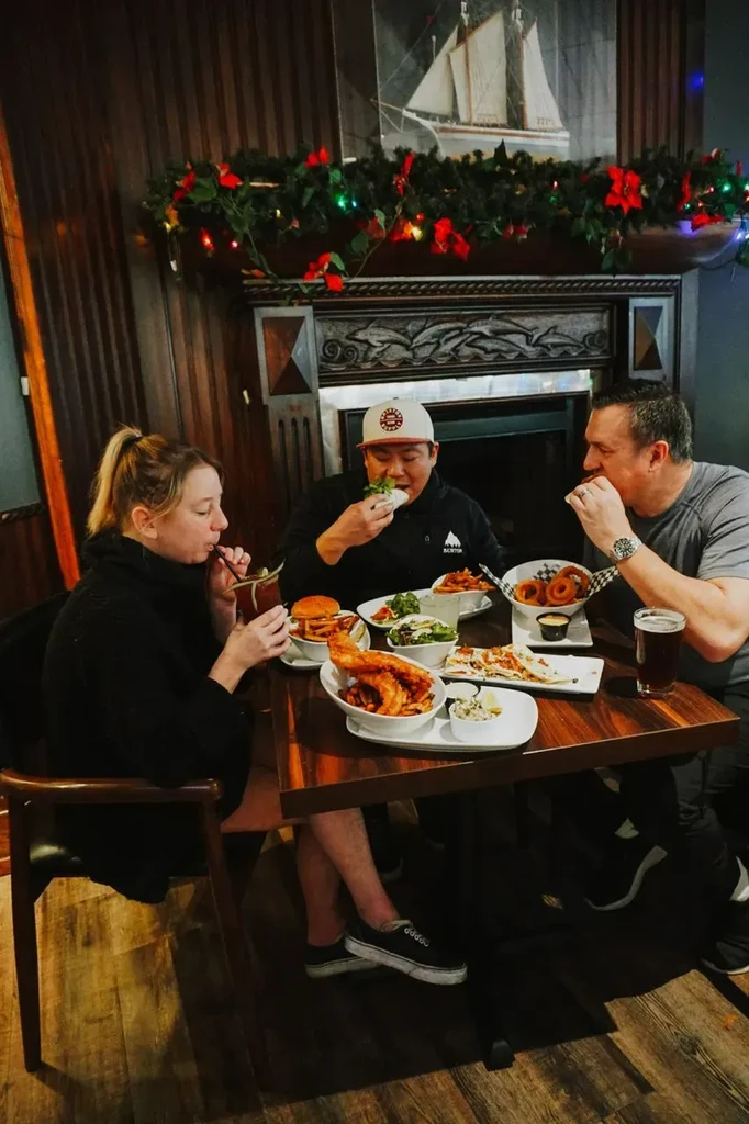 Two men and a woman eating meals and drinks in a festive pub.
