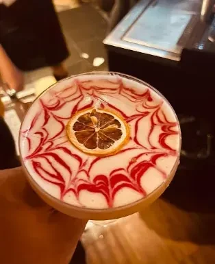 Top-down cocktail with creamy foam, red swirls, and dried orange slice.