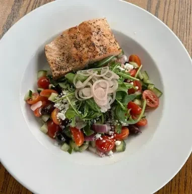 Grilled salmon fillet on a vibrant Greek salad with feta and olives.
