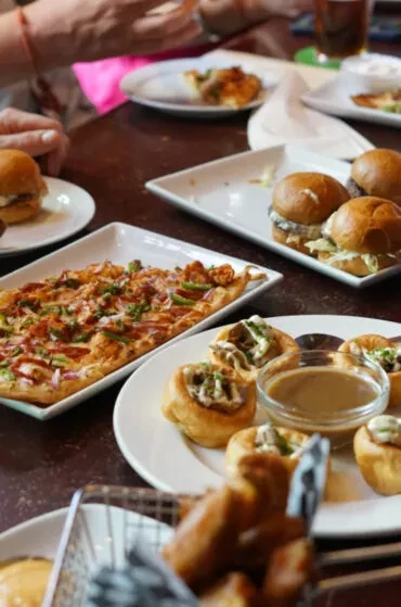 Table filled with appetizers: flatbread, sliders, fries, and filled pastries.