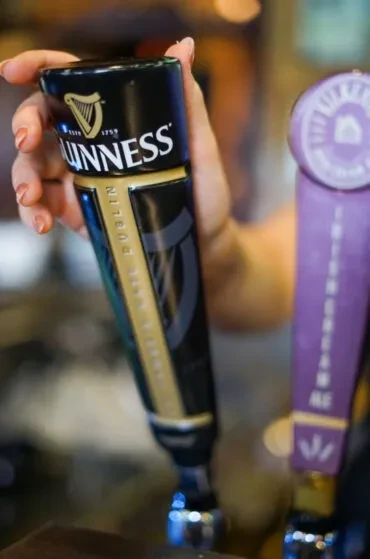 Hand pulls a black and gold Guinness beer tap handle.