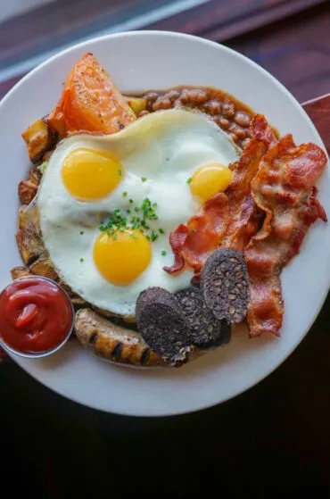 A full English breakfast with fried eggs, bacon, sausage, and black pudding.