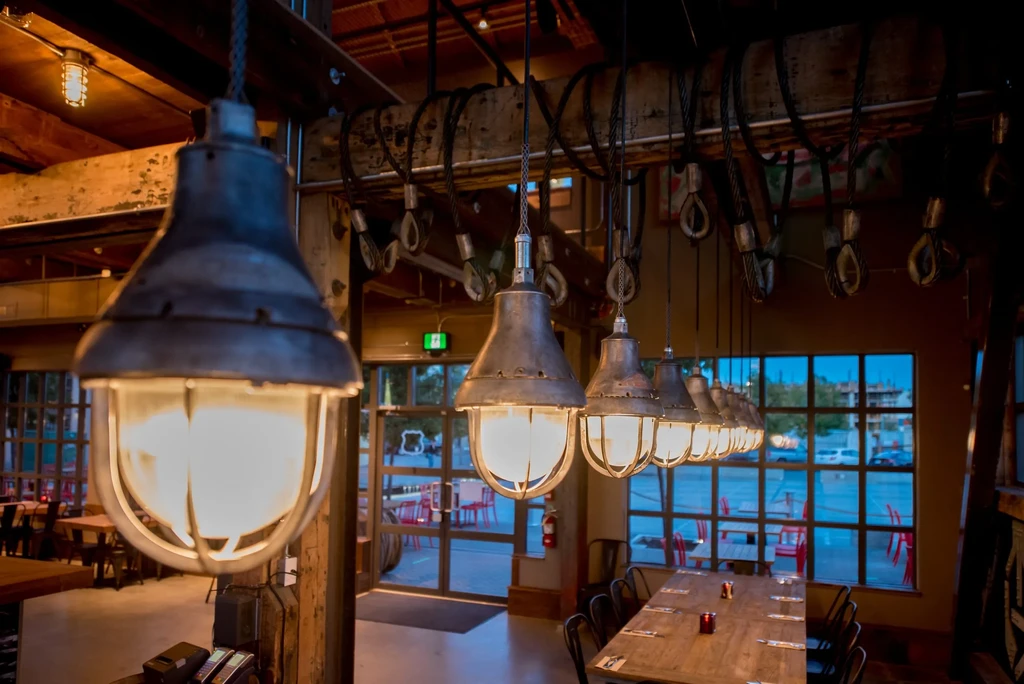 Industrial caged lamps illuminate a rustic restaurant with a communal wooden table.