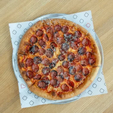 Round pepperoni pizza with grated cheese on a silver metal pan.