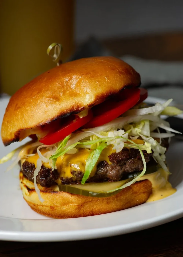 Close-up cheeseburger with melted cheddar, lettuce, tomato, pickles on plate.