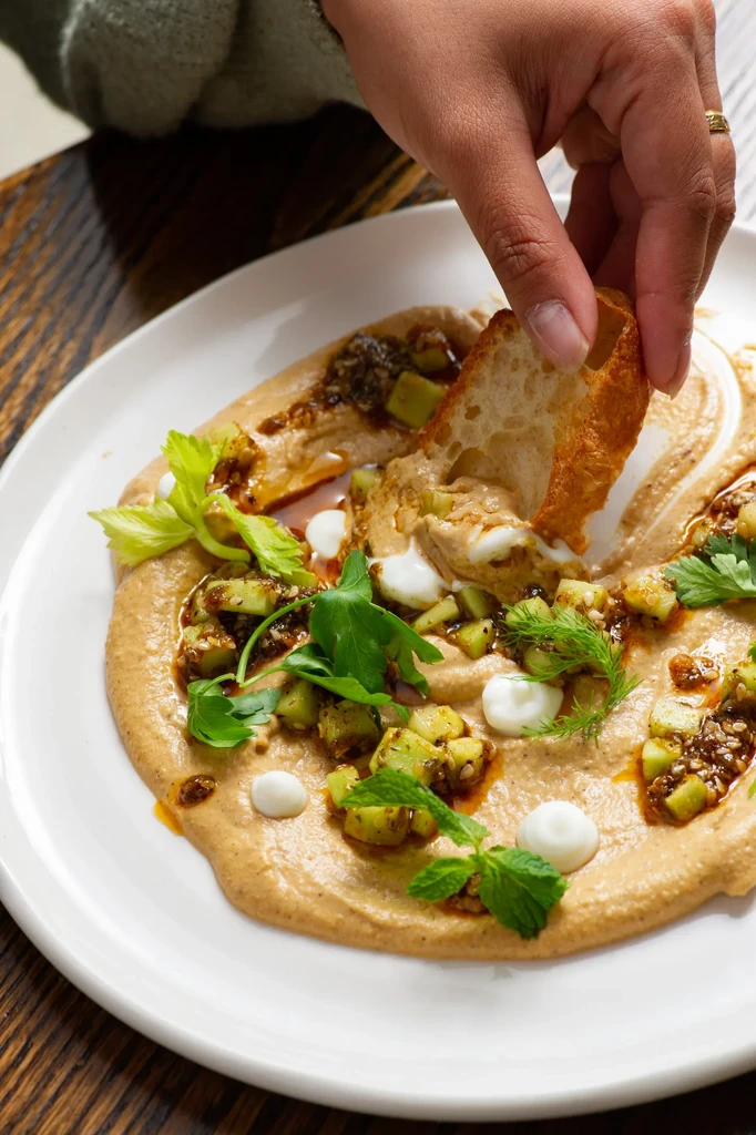 Creamy dip garnished with apples, relish, herbs; hand dips crusty bread.