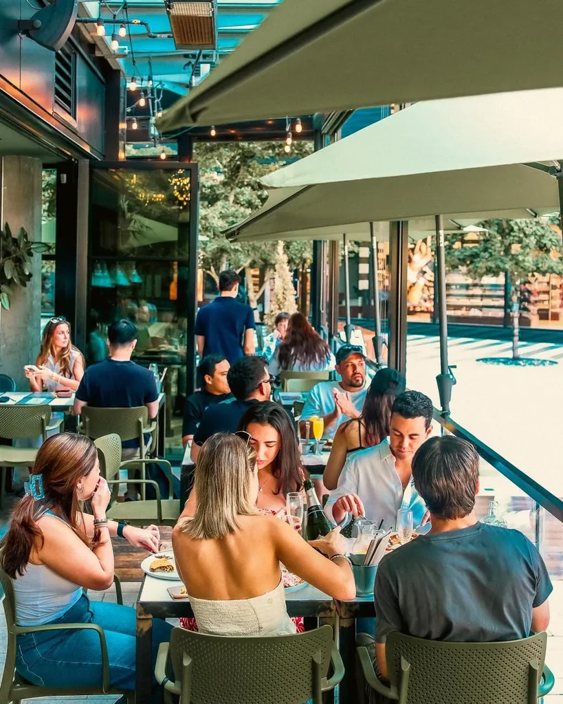 Elevated view of bustling outdoor restaurant, woman pours champagne, urban scene.