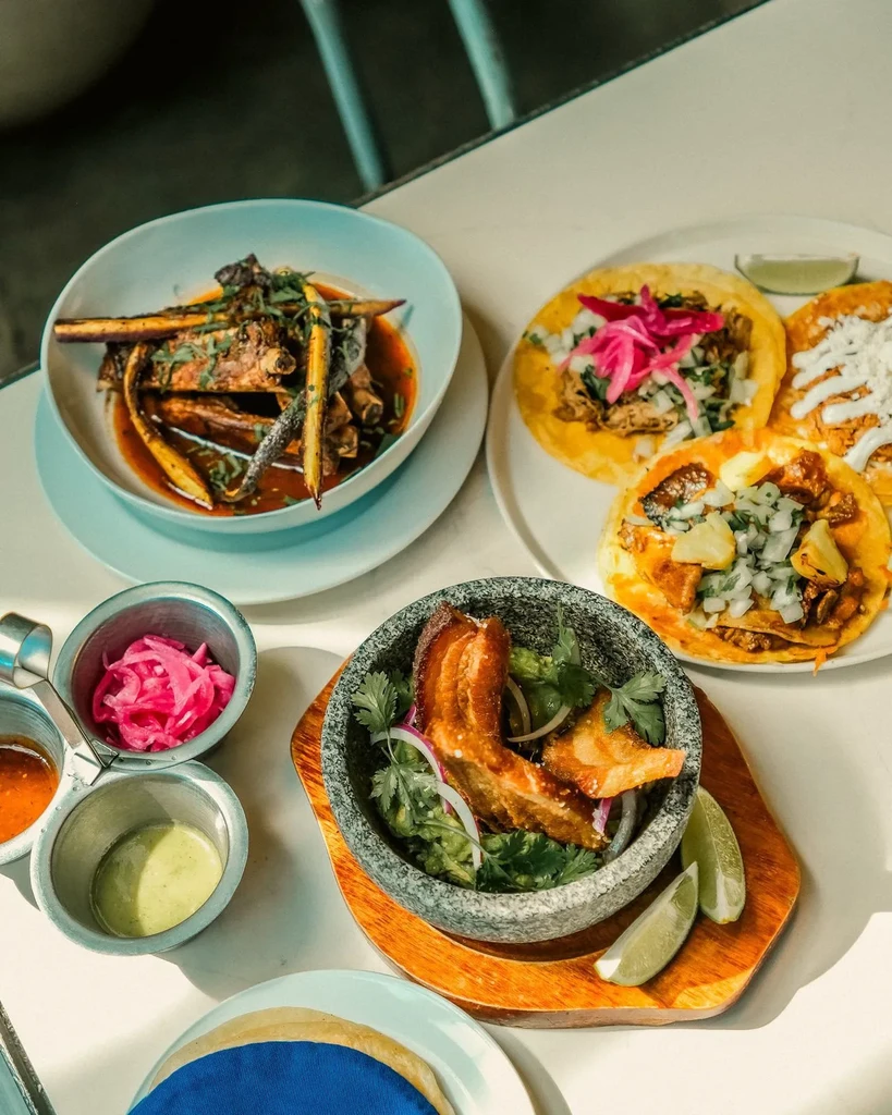 Vibrant tabletop of Mexican food: tacos, braised meat, guacamole with chicharrón.