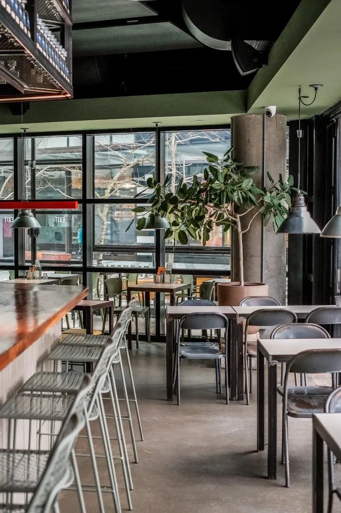 Empty industrial-chic restaurant interior with a bar, tables, and olive green walls.