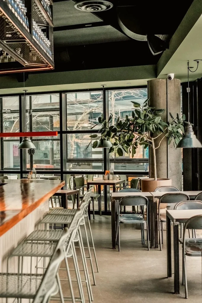 Modern industrial restaurant interior with long bar and large windows.