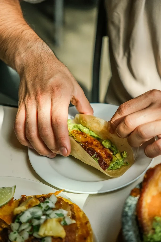Close-up of hands holding a taco with golden filling and green salsa.