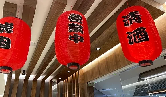 Three red Japanese lanterns with Kanji hang from a wood-slatted ceiling.