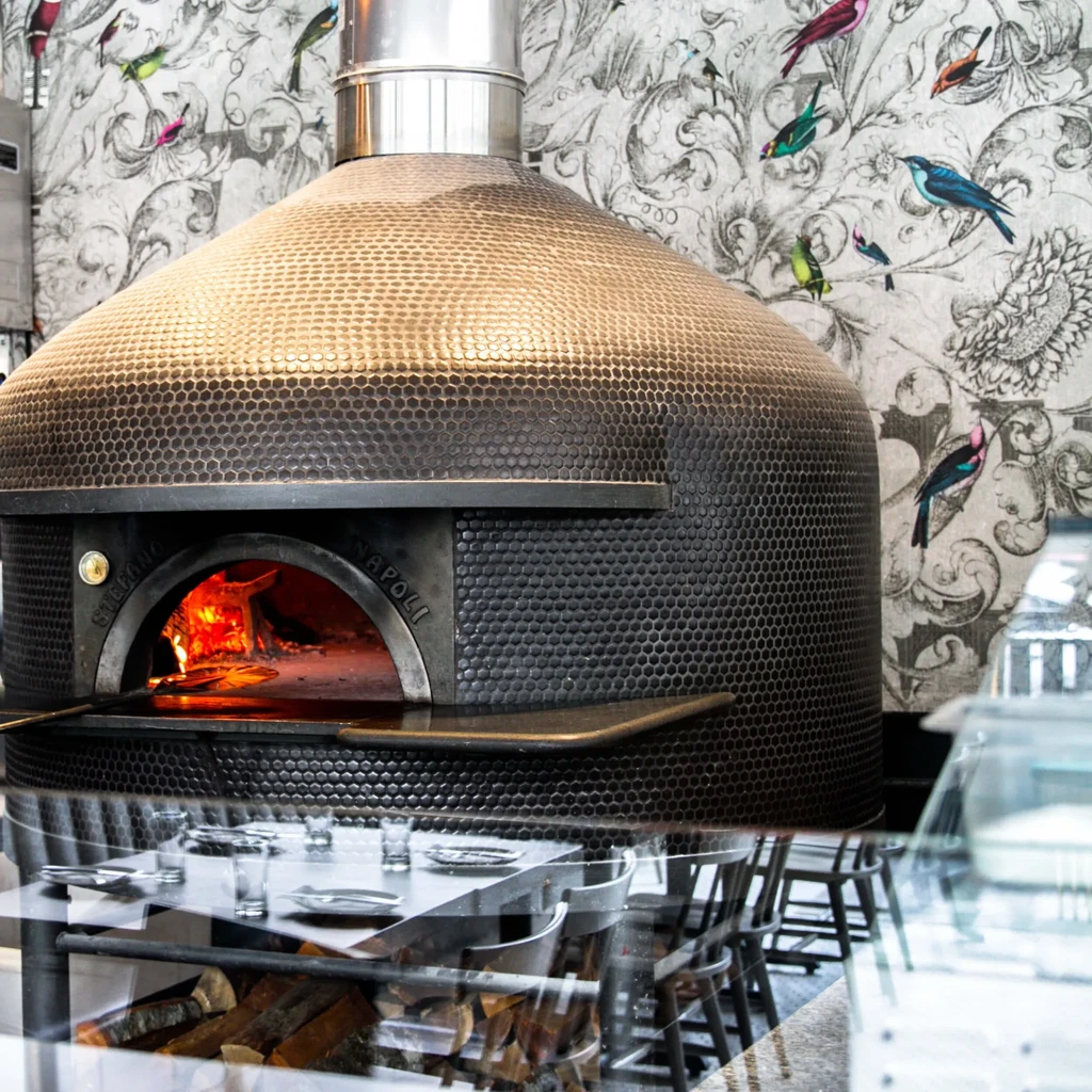 Restaurant interior with large hammered metal pizza oven and glowing fire.