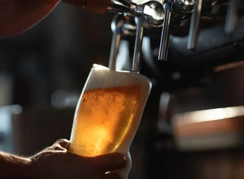 Hand fills a tilted glass with golden beer from a tap.